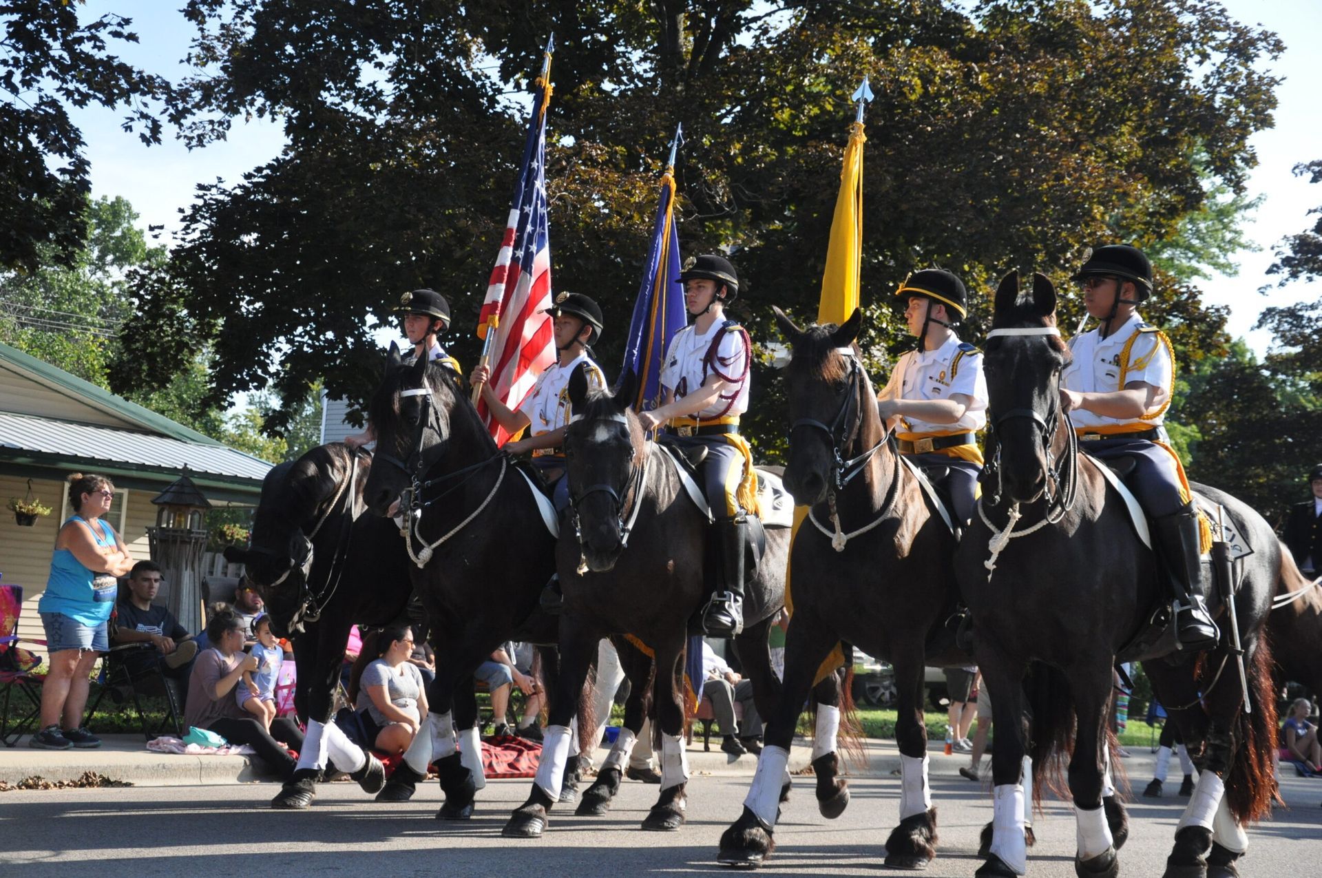 Mounted police officers in uniform carrying flags in a parade on a sunny street.