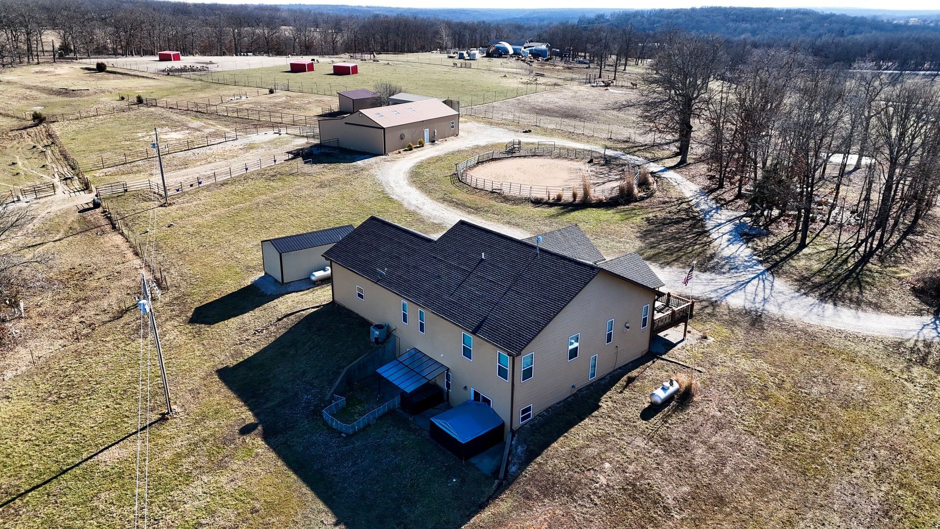 Aerial view of a farm with a house, barns, a circular pen, and fields under a blue sky.