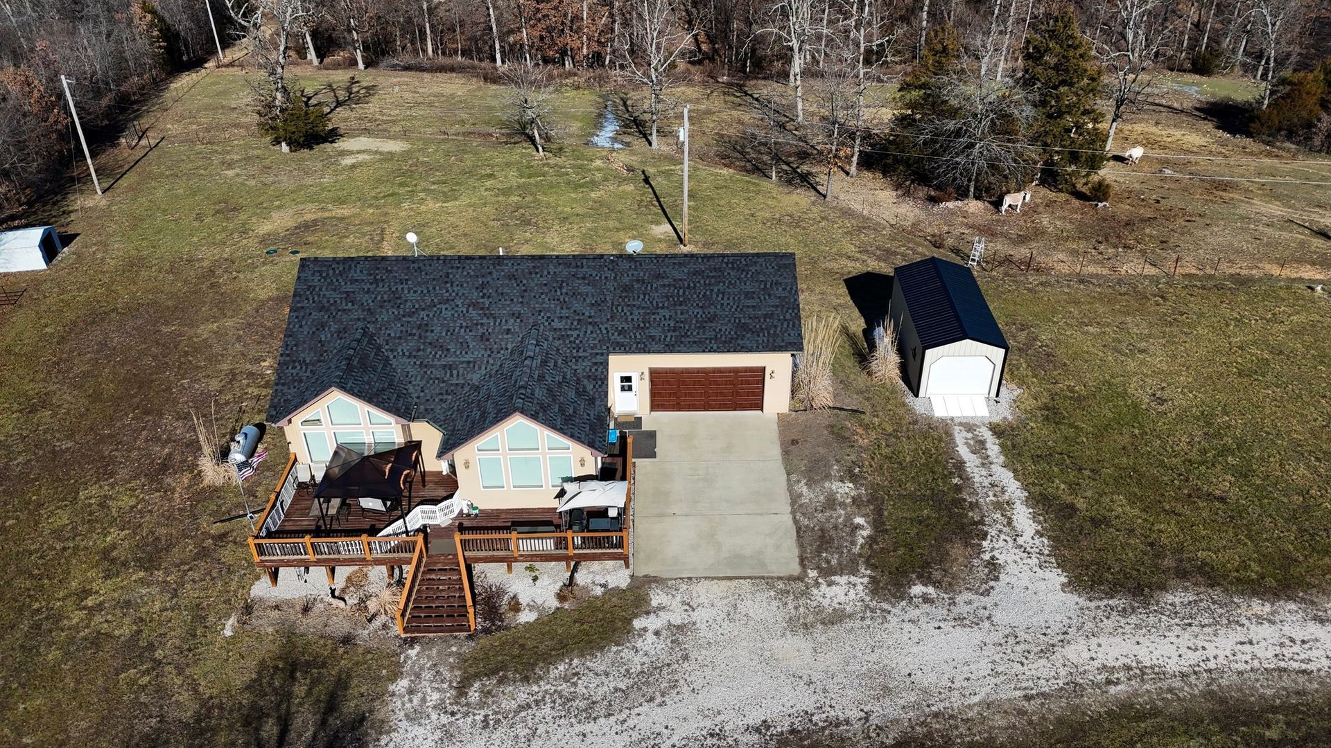 Aerial view of a house with a dark roof and attached garage, next to a detached carport on a hillside.