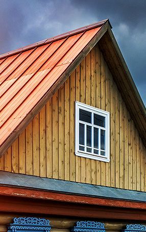 Orange roof and wooden gable wall with a window against a dark, cloudy sky.