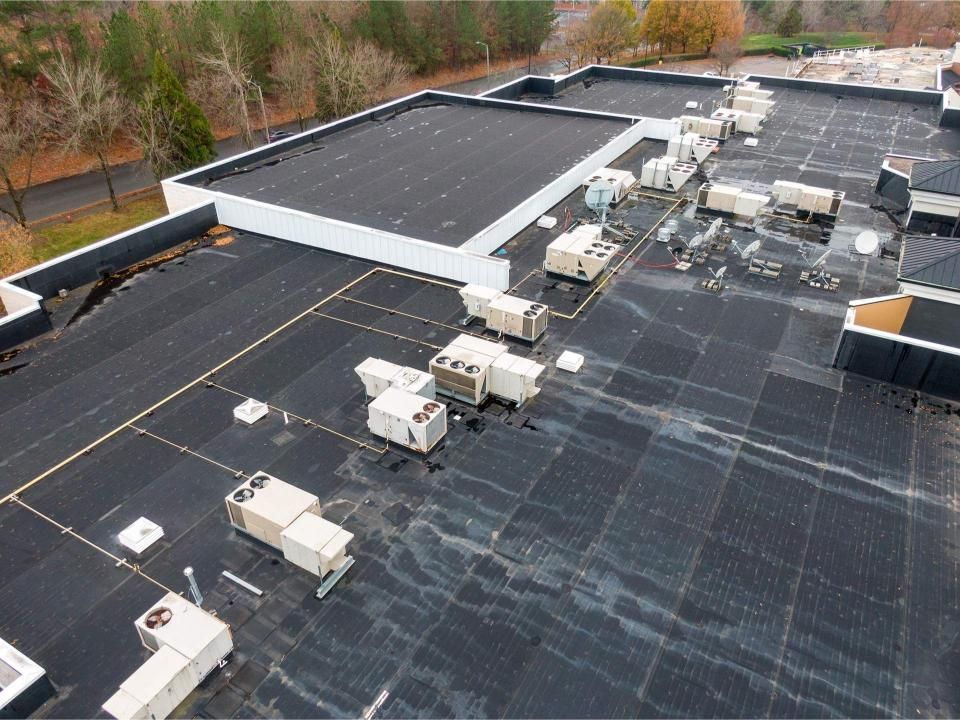 Overhead view of a flat commercial roof with HVAC units and dark roofing material.