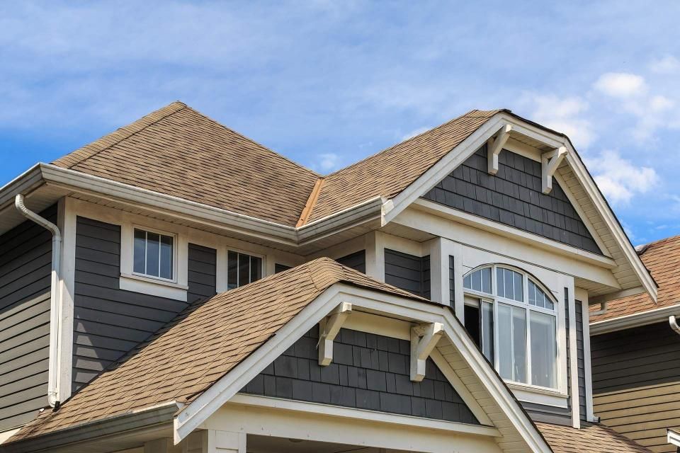House with gray siding and brown roof under a blue sky.