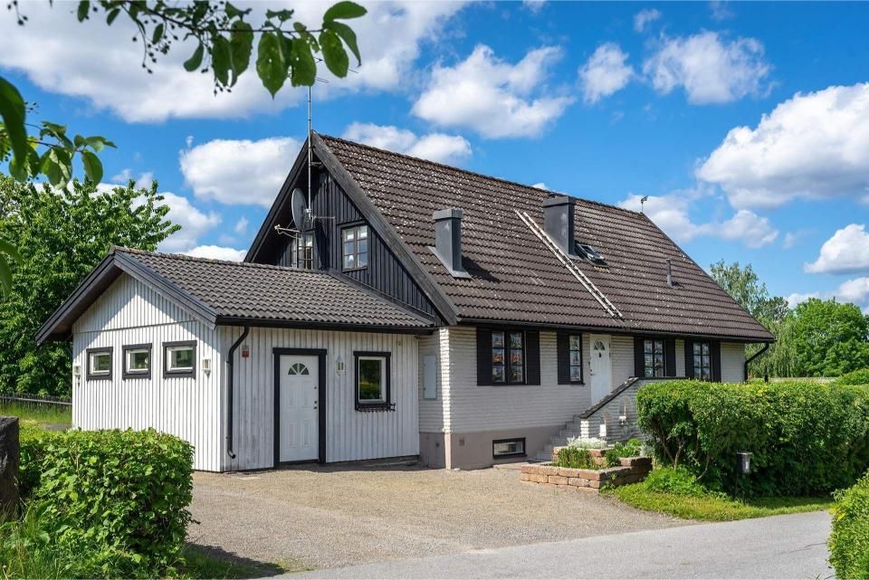 Two-story house with black trim, a gray roof, and a white garage under a blue sky.