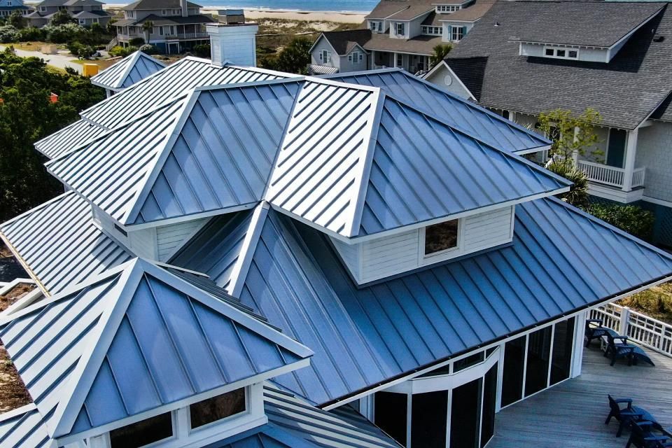 Blue metal roof on a white house with multiple gables near the ocean.