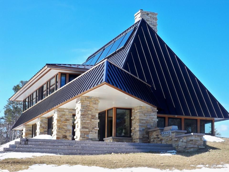A modern house with a black angular roof, stone columns, and large windows on a sunny day.