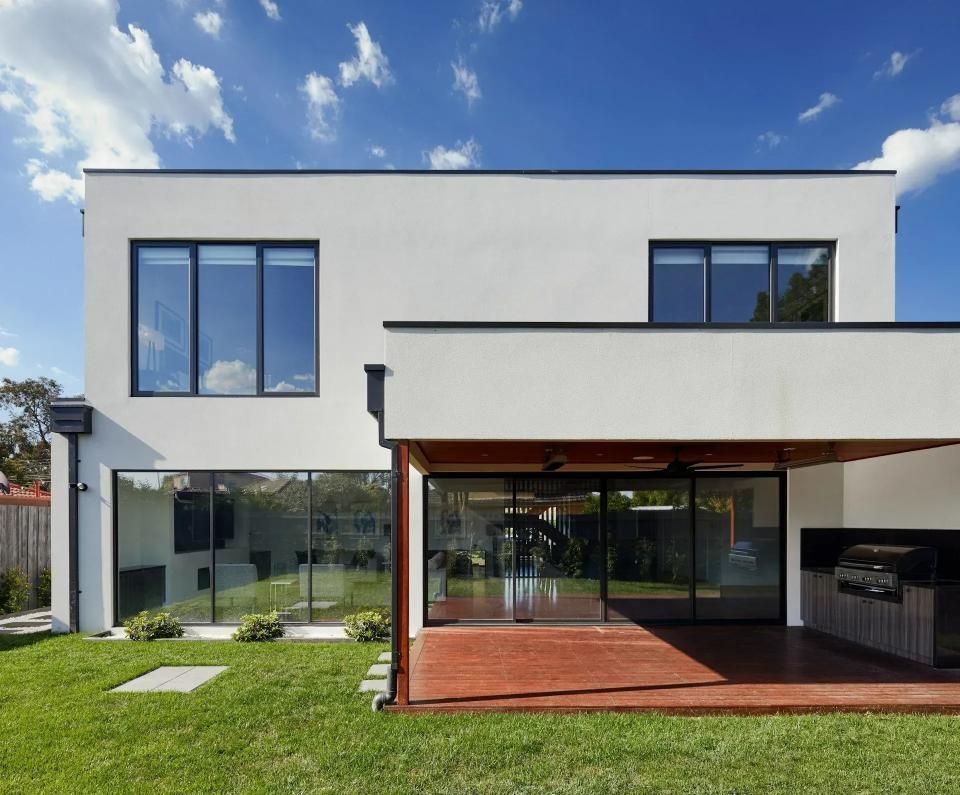 Modern white house with dark framed windows, glass doors, and a red-toned outdoor patio.