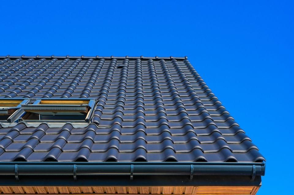 Dark tile roof with gutter, against a bright blue sky.