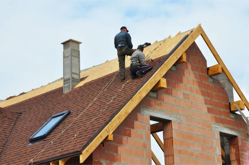 Two roofers working on a red-tiled roof of a brick house under construction.