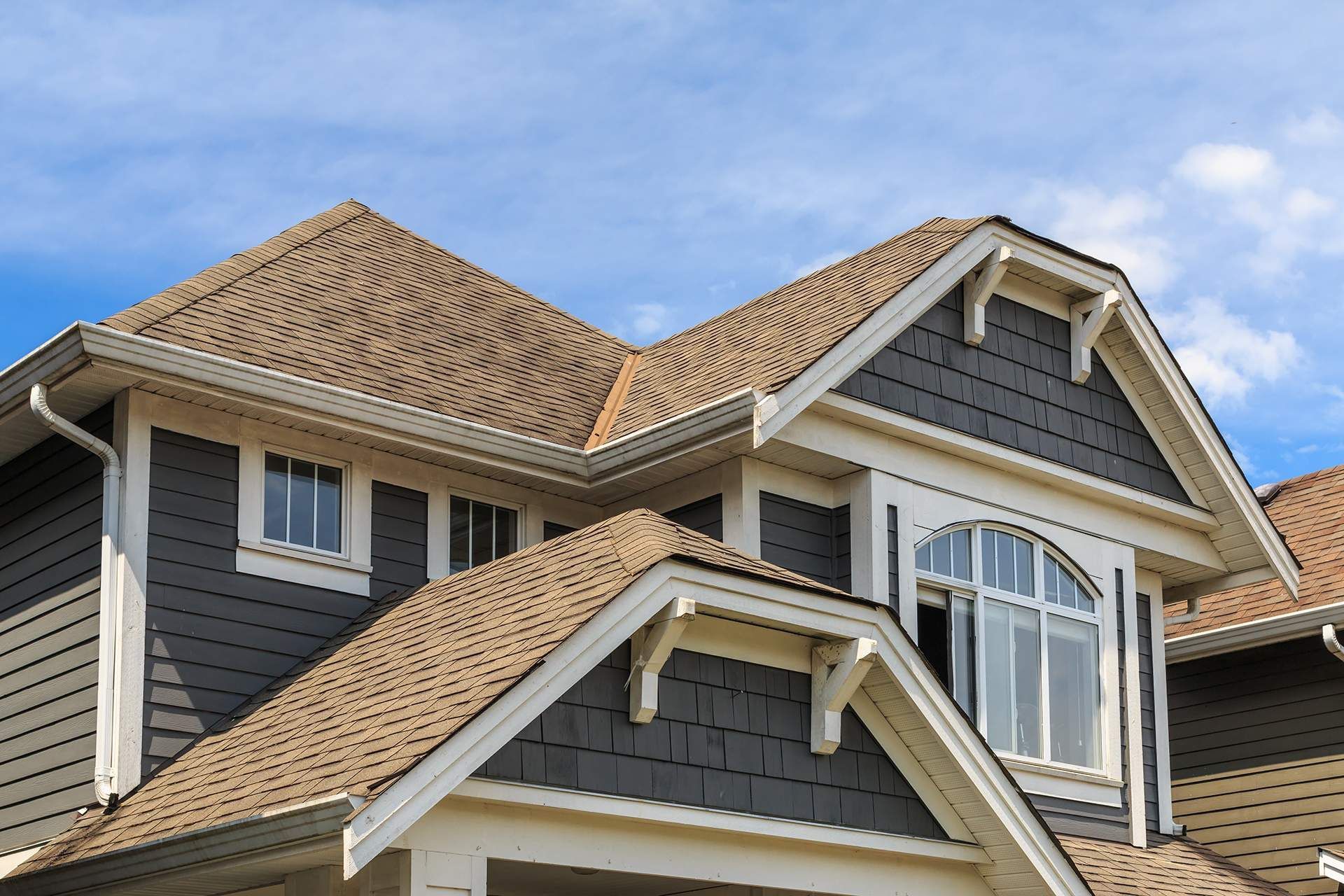 House with gray siding and brown roof under a blue sky.