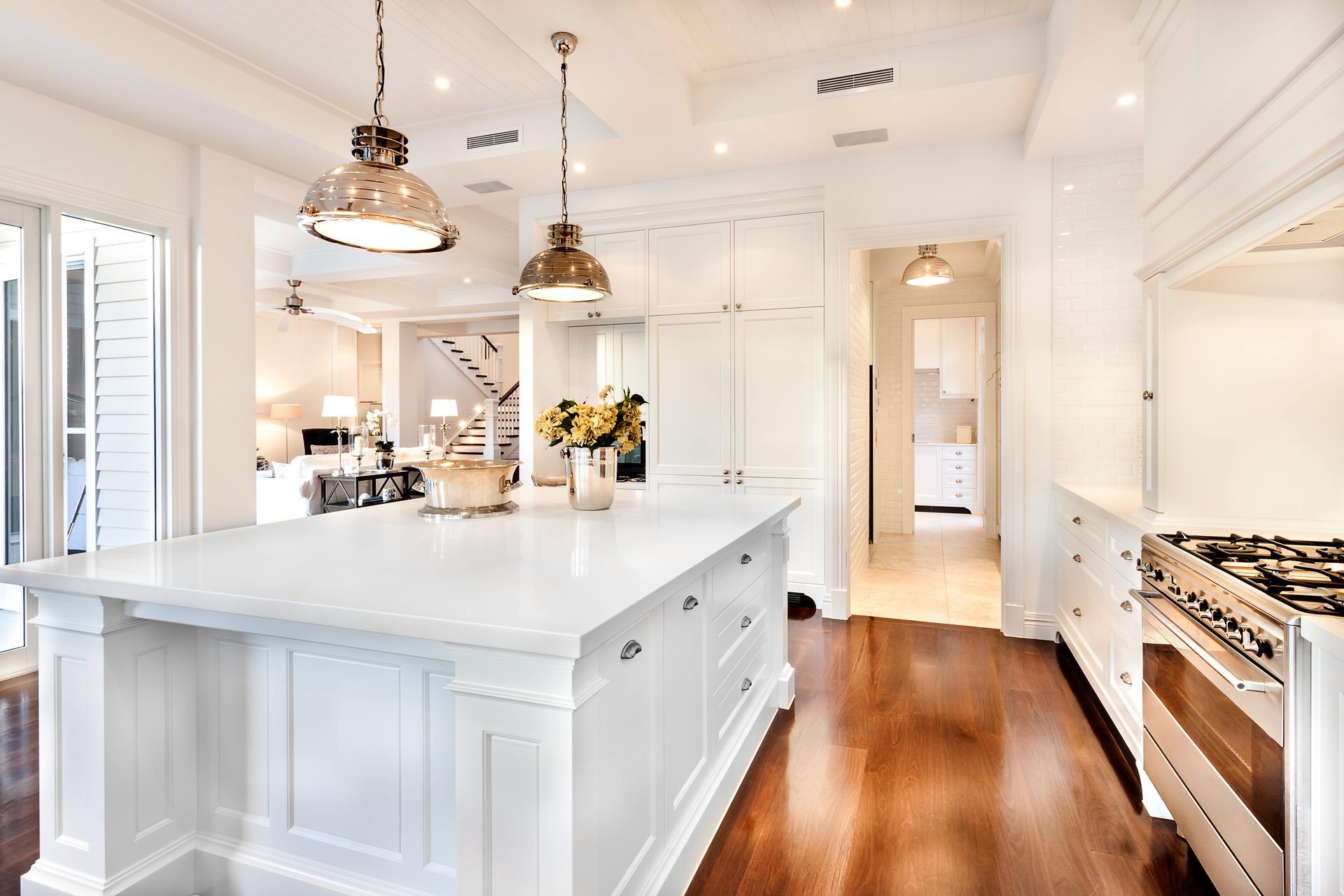 Elegant white kitchen with island, wood floors, and pendant lights.