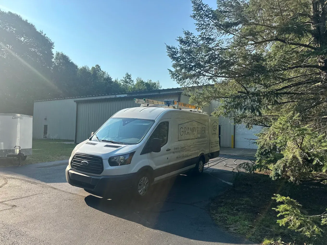 White utility van parked in front of a gray industrial building with trees and a blue sky in the background.