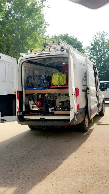 White work van with open doors, revealing tools and equipment. Outdoors, sunny day.