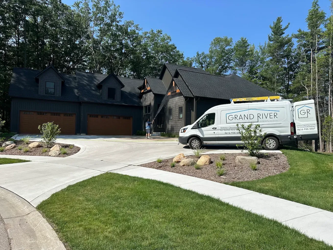 Black house with brown garage doors, service van in driveway, on sunny day.