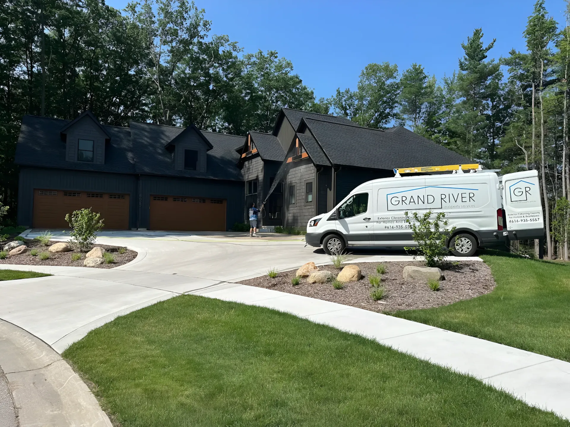Black house with brown garage doors, a white van in the driveway, on a sunny day.