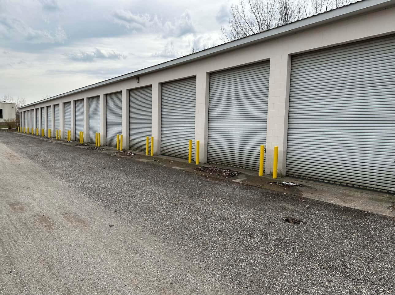 Storage units with wavy-patterned doors, gray gravel path, yellow bumpers, overcast sky.
