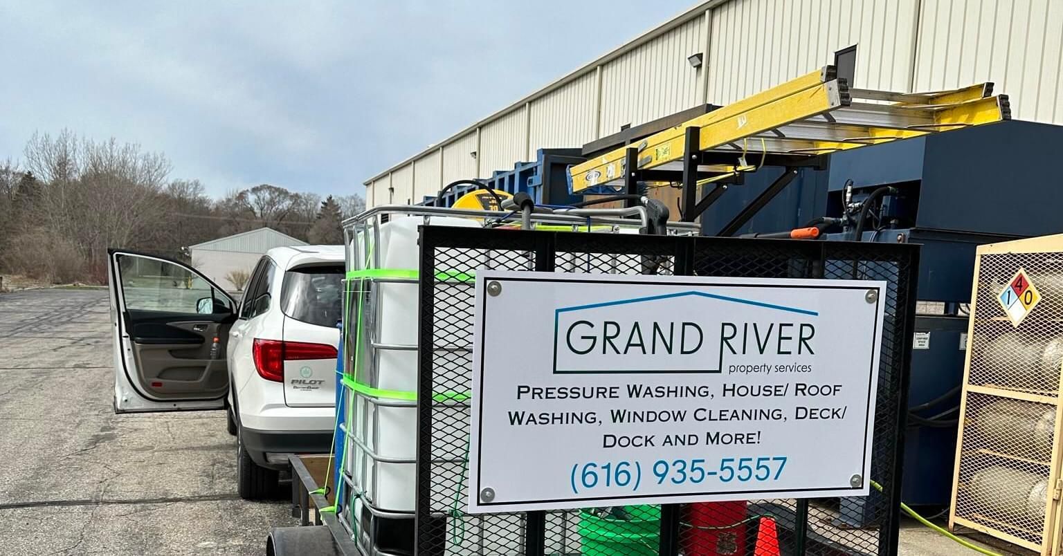 A trailer with pressure washing equipment. Includes a white SUV. Sign for Grand River Pressure Washing.