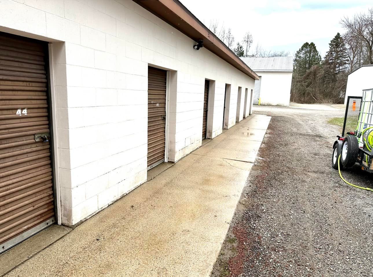 Row of storage units with brown doors and a concrete walkway.