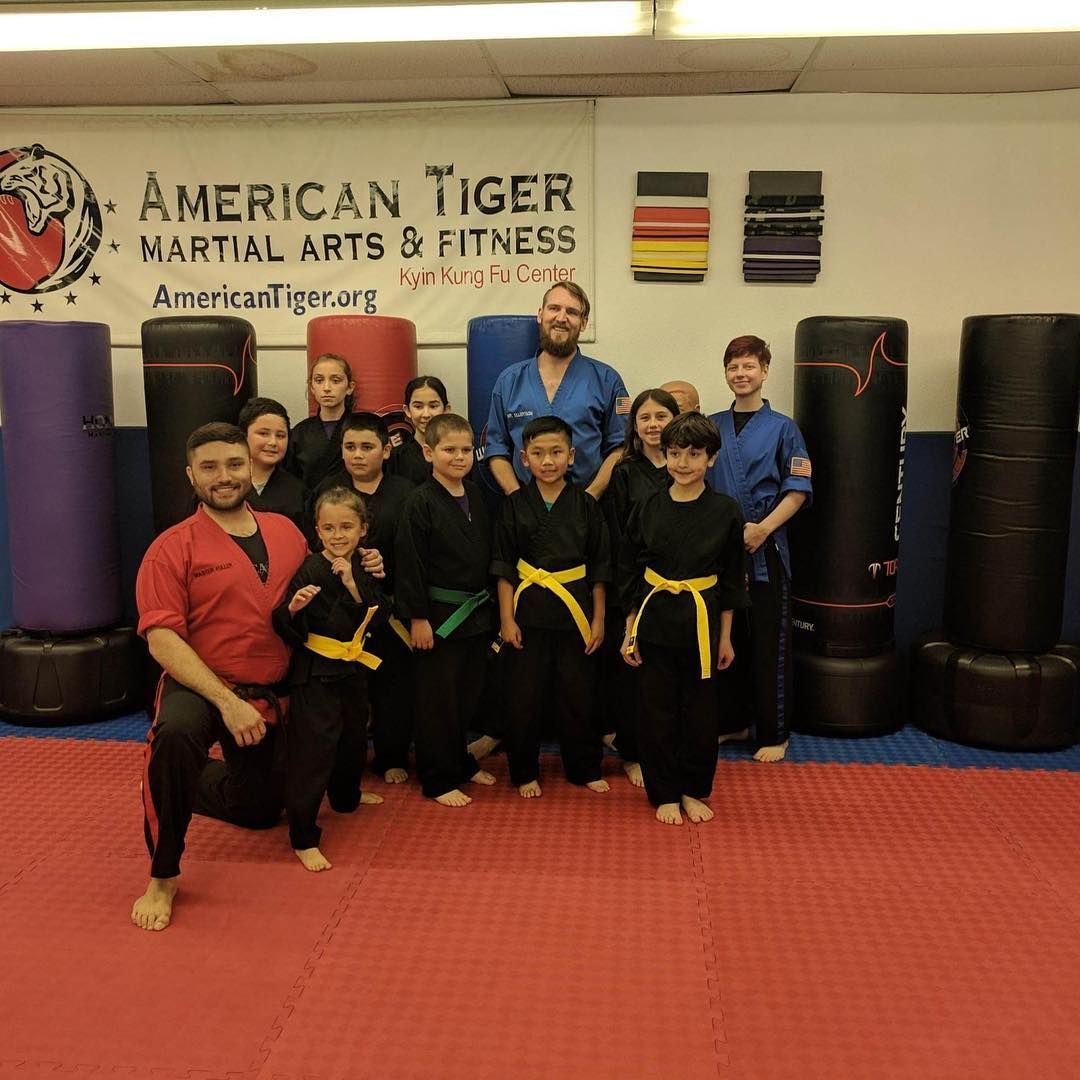 A group of people posing for a picture in front of a sign that says american tiger martial arts & fitness