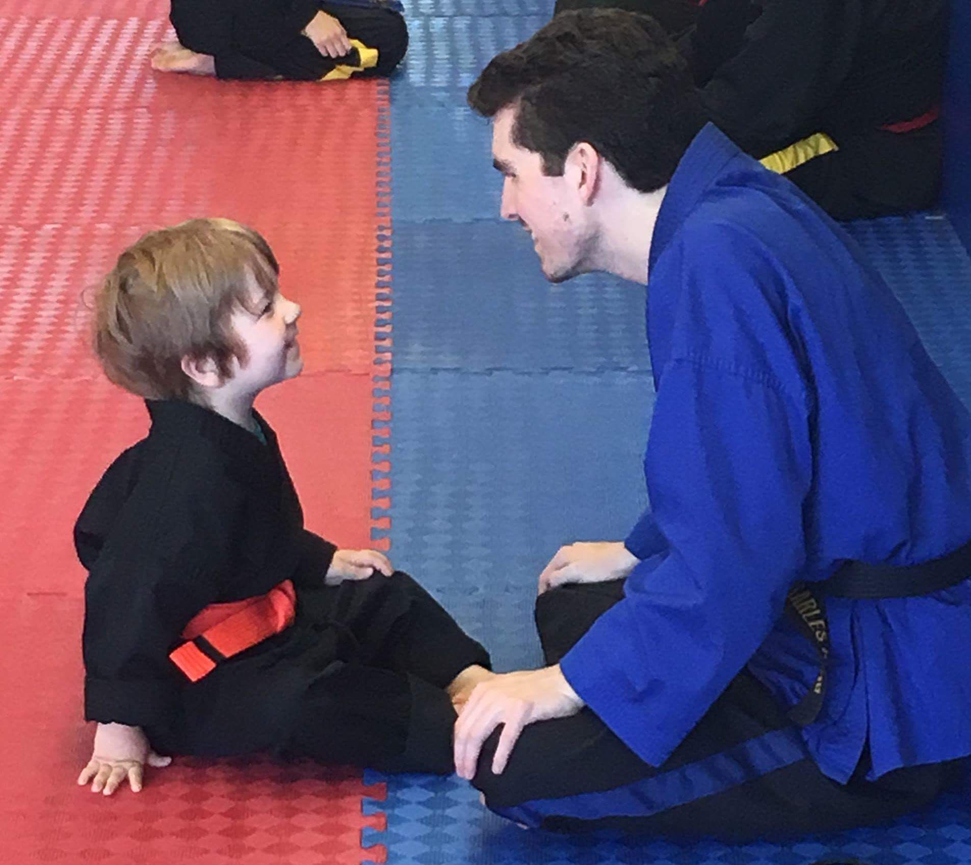 A man in a blue jacket is kneeling down next to a little boy in a black uniform
