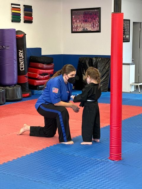 A woman is kneeling down next to a child in a martial arts gym.