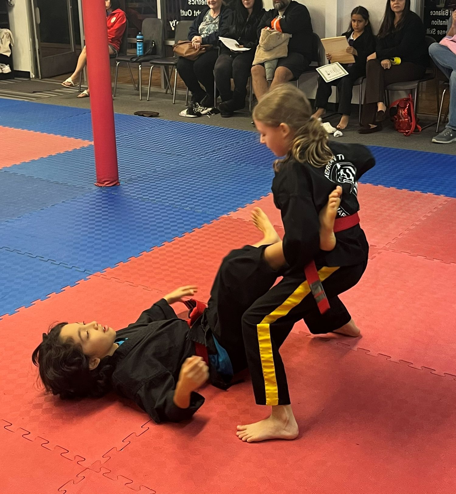 Two children sparring on red and blue mats at an indoor martial arts event