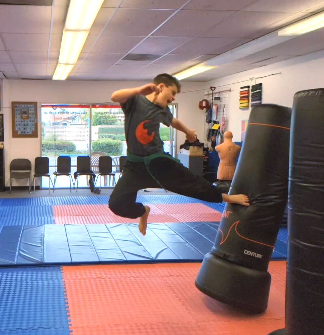 A young boy is jumping in the air in a martial arts gym