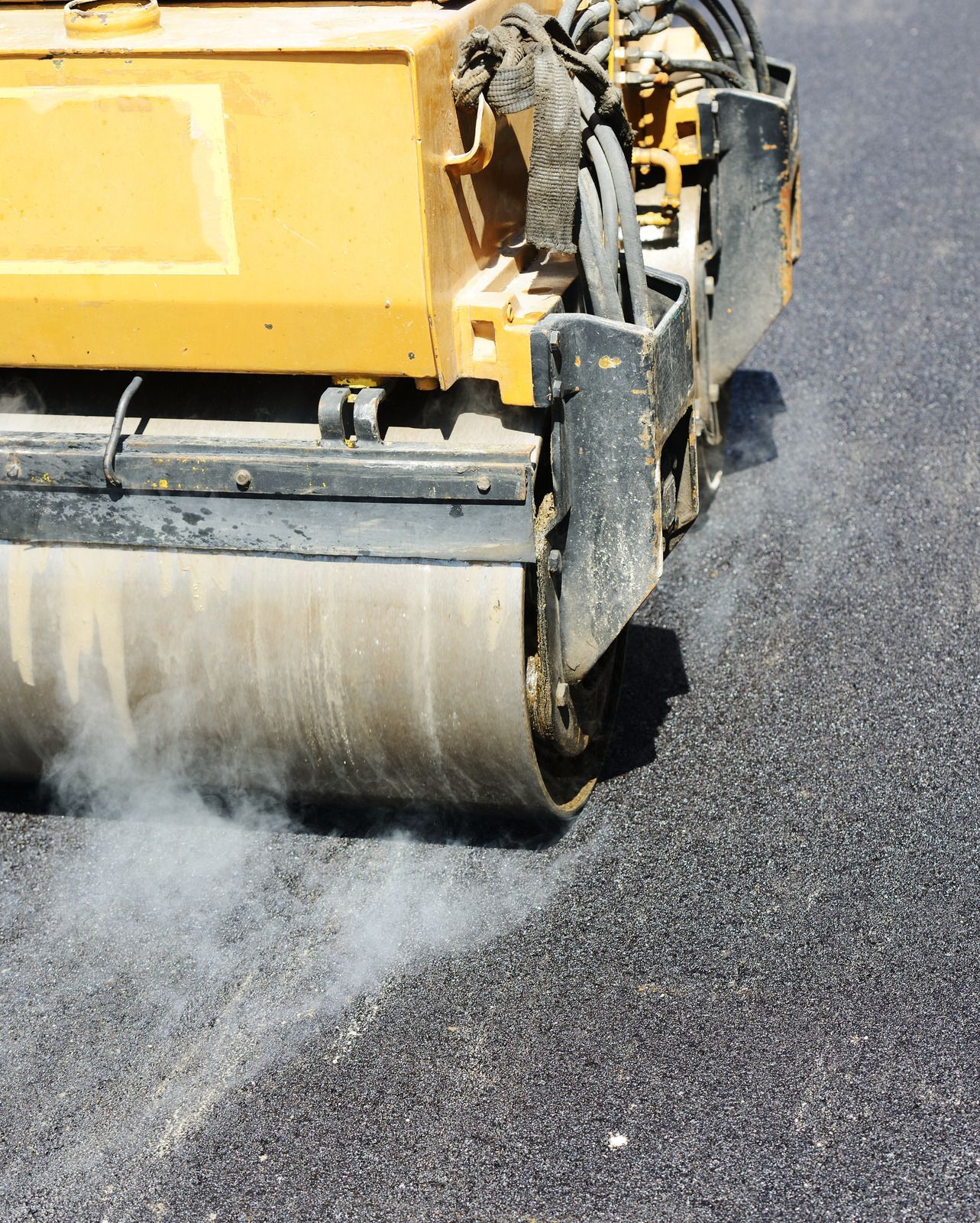 A yellow roller is rolling asphalt on a road