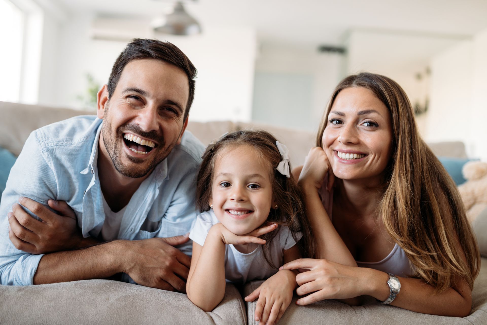 A family is laying on a couch and smiling for the camera.