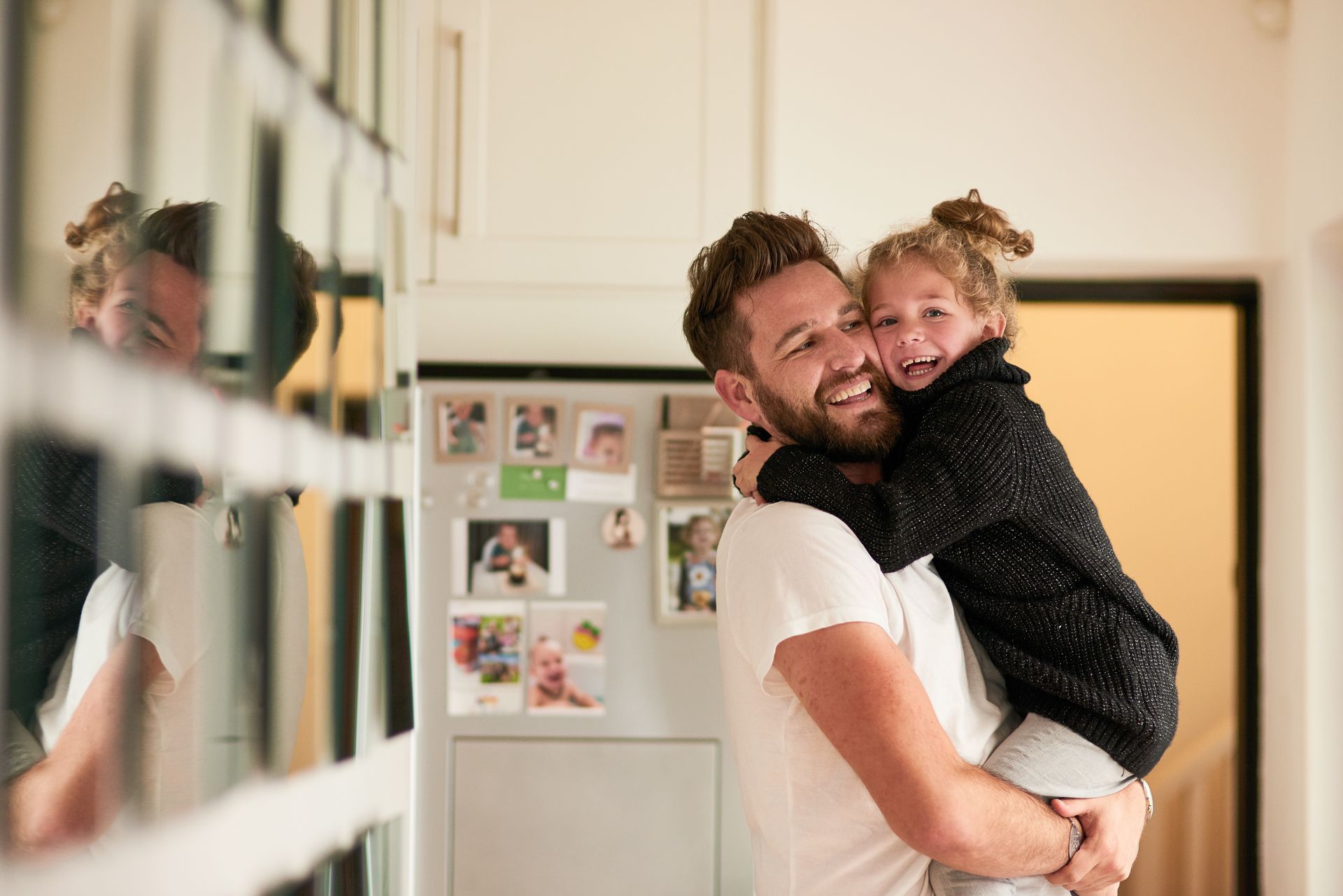 A man is carrying a little girl on his back in a kitchen.
