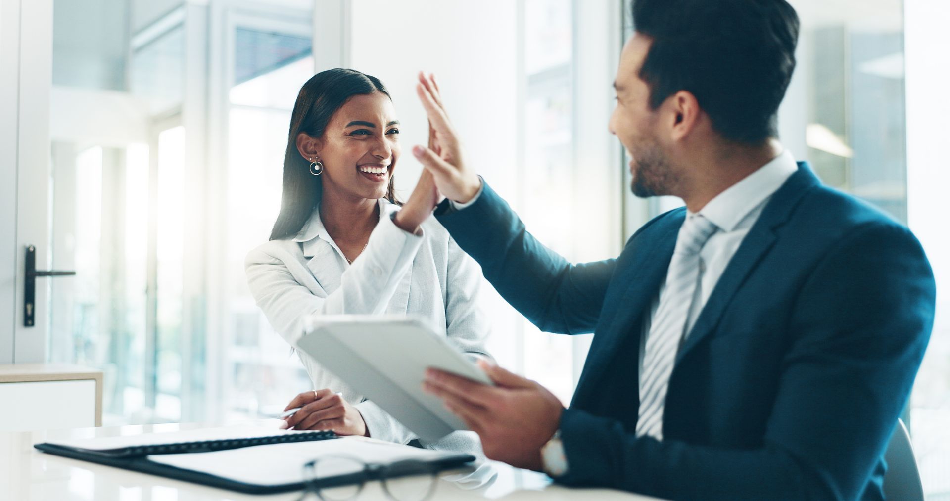 A man and a woman are giving each other a high five while sitting at a table.