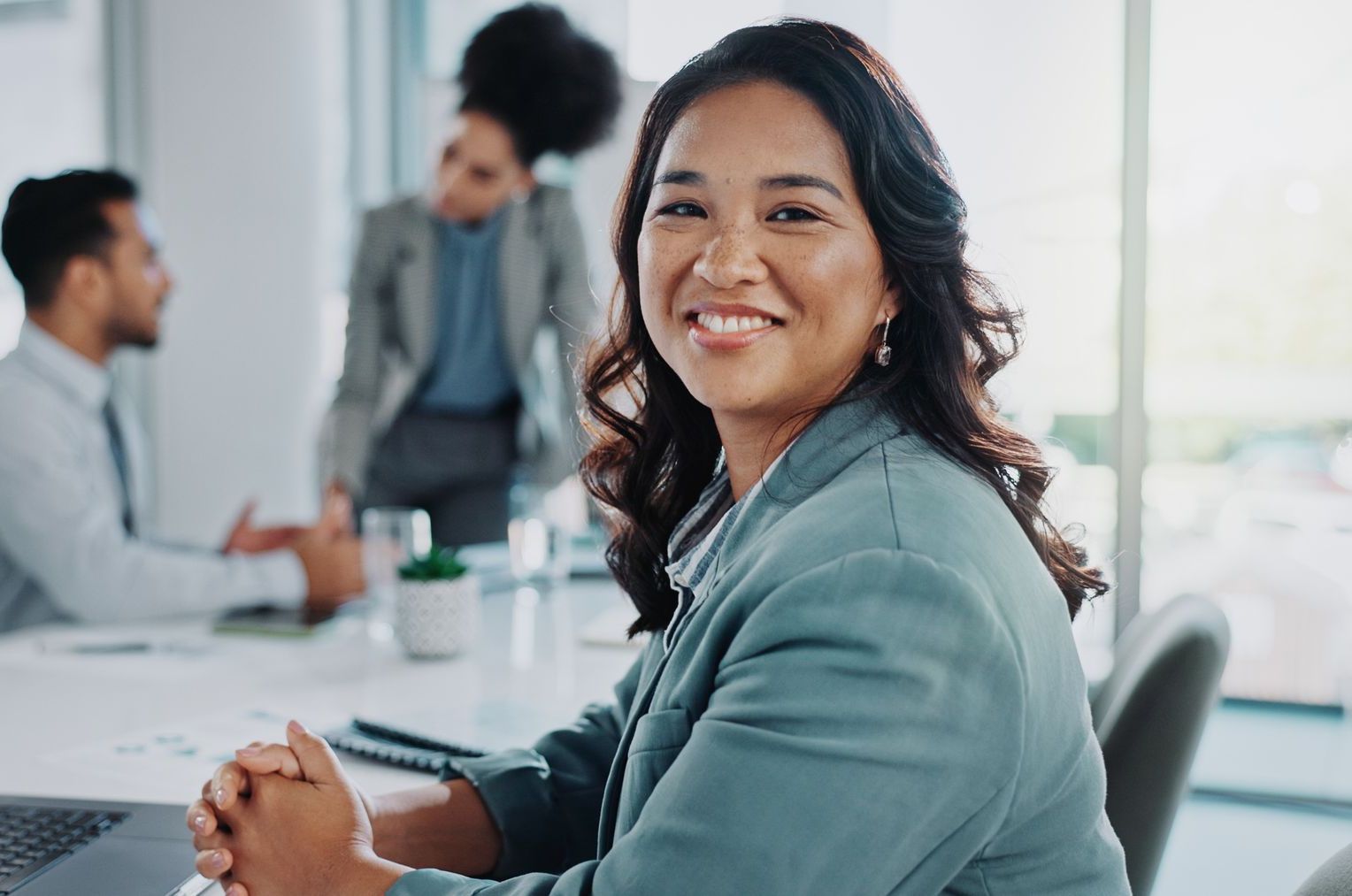 A woman is smiling while sitting at a desk in front of a laptop computer.