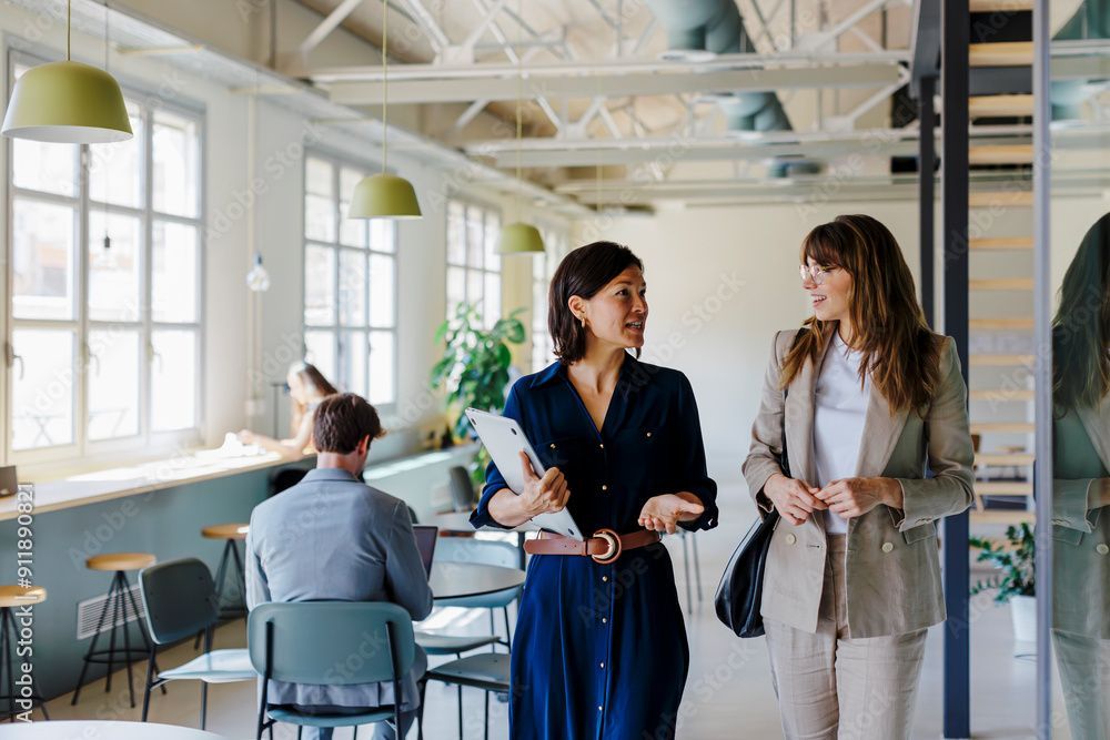 Two women are walking in an office and talking to each other.