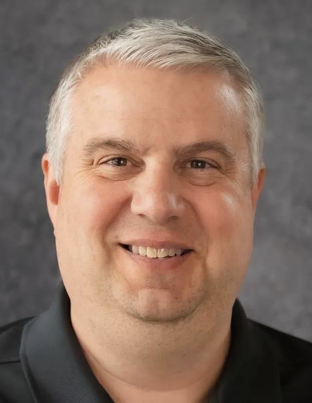 A man with gray hair and a black shirt is smiling for the camera.