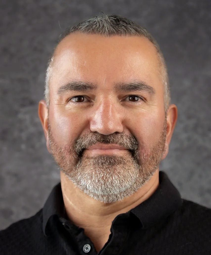 A man with a beard is wearing a black shirt and smiling for the camera.