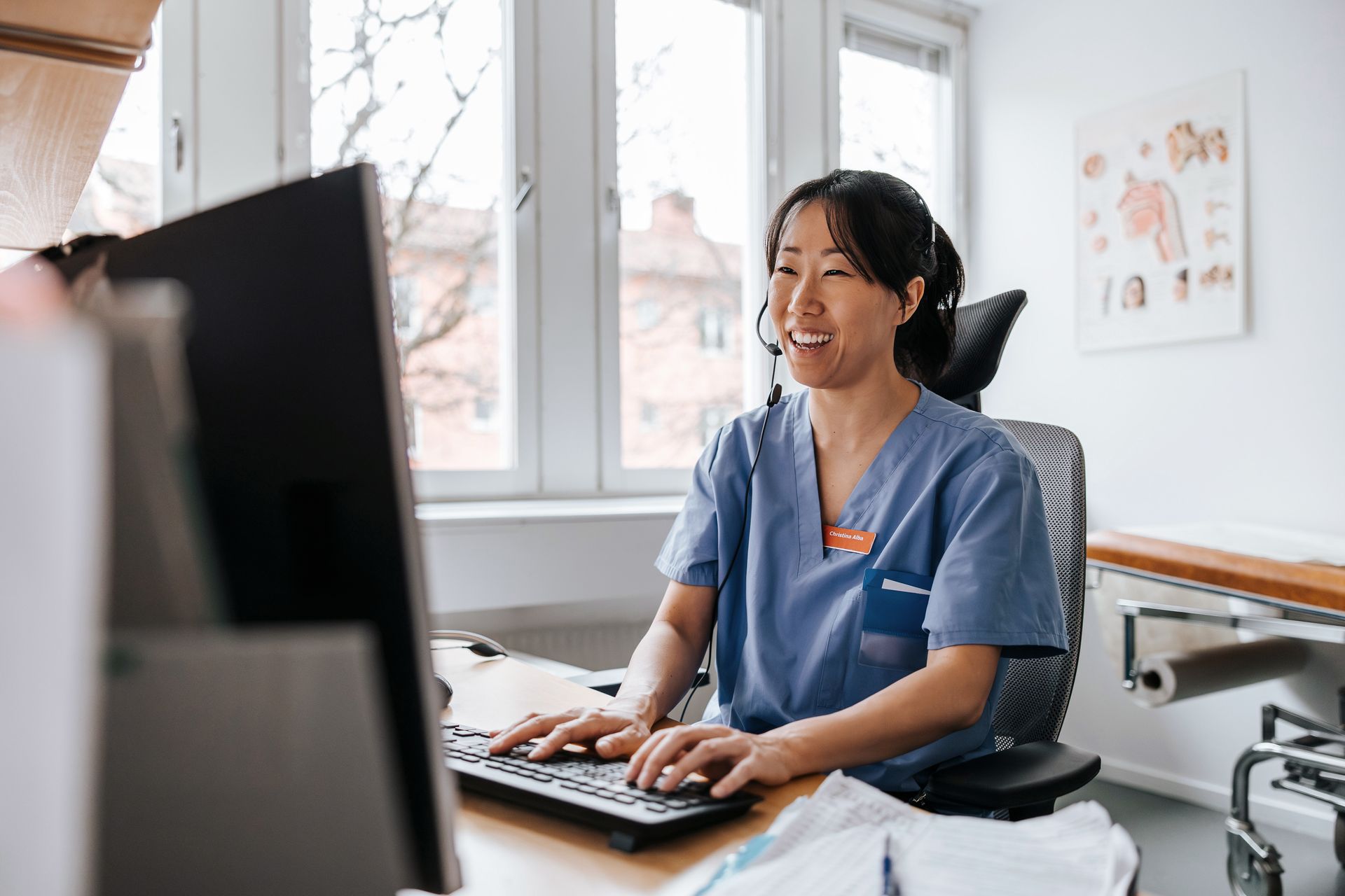 A nurse is sitting at a desk in front of a computer.