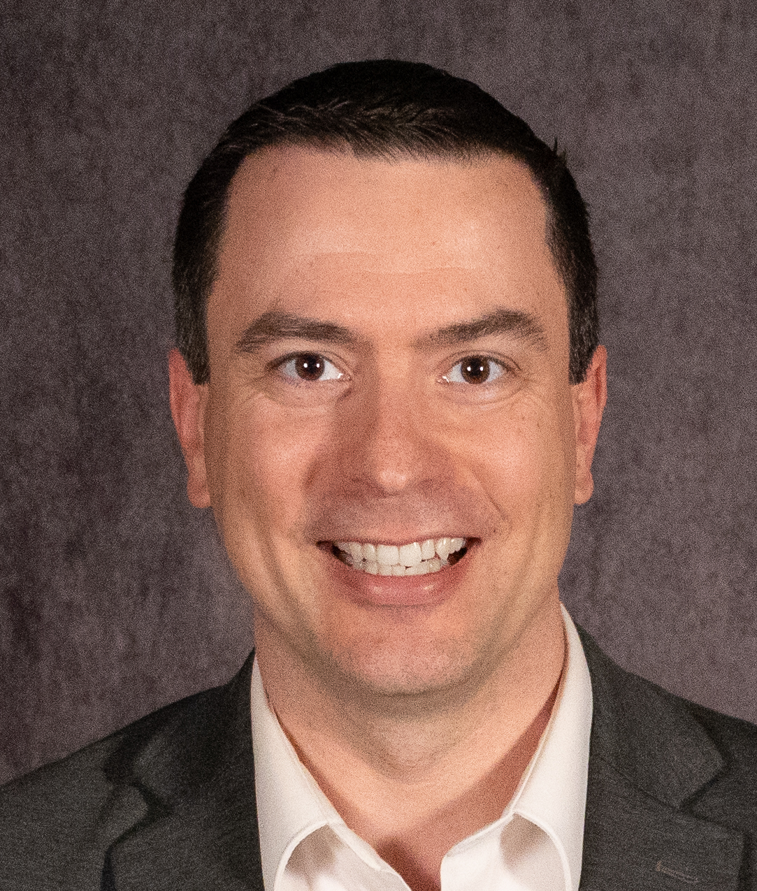 A man wearing glasses and a black shirt is smiling for the camera.