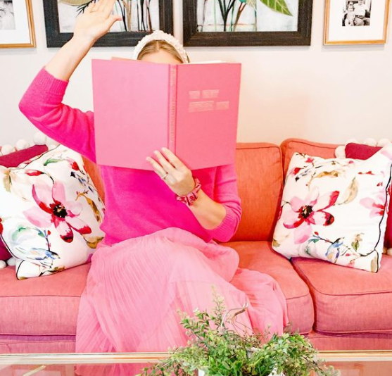 A woman is sitting on a pink couch reading a pink book