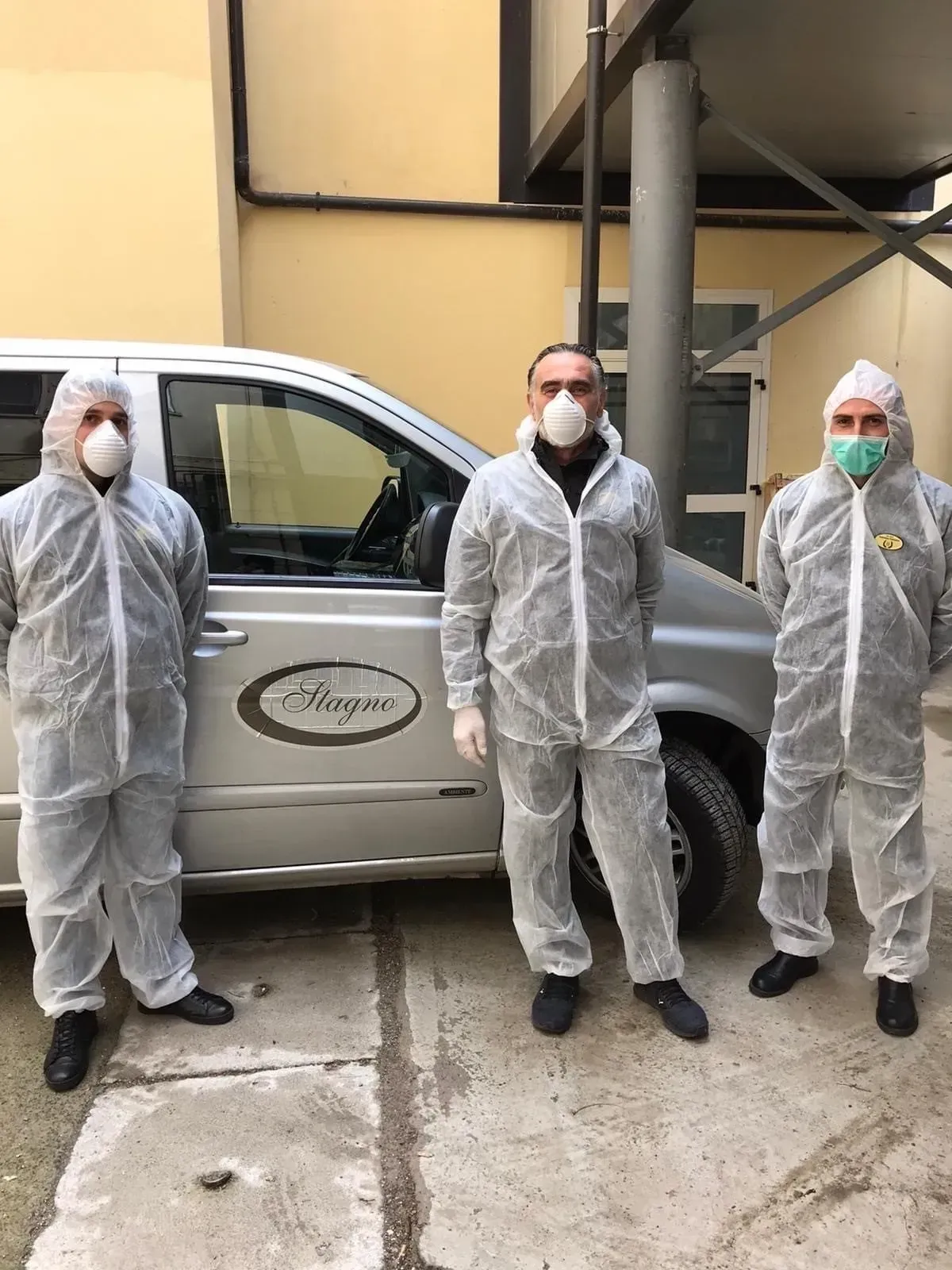 Tre uomini che indossano tute protettive e maschere sono in piedi davanti a un furgone.