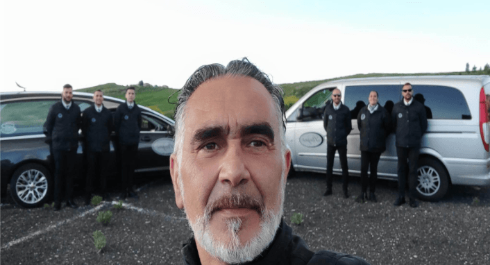 Un uomo con la barba è in piedi di fronte a un gruppo di uomini fermi davanti ai furgoni.