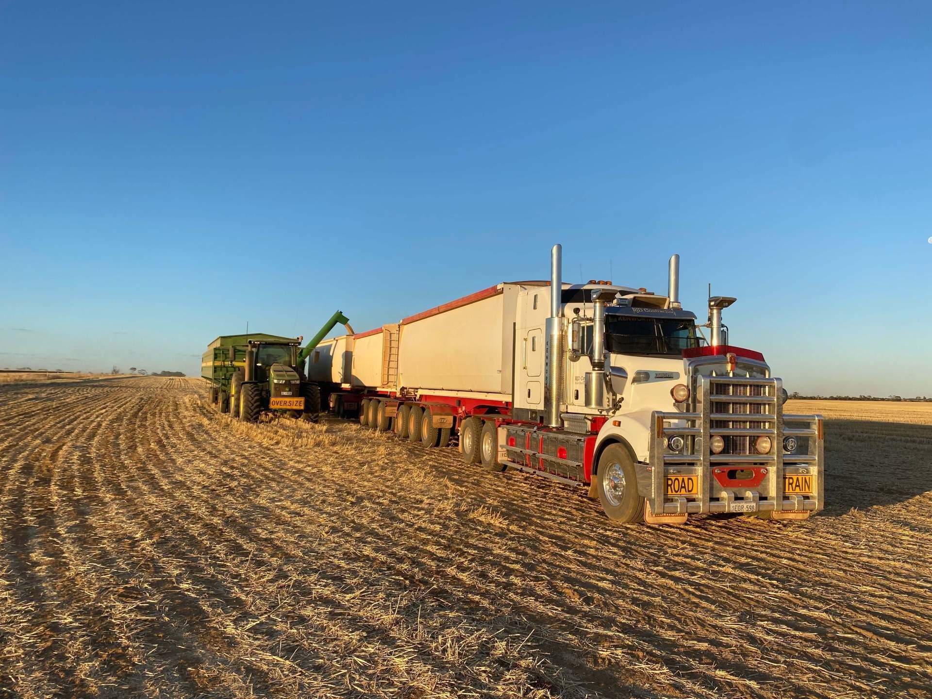A semi truck is parked in a field next to a tractor.