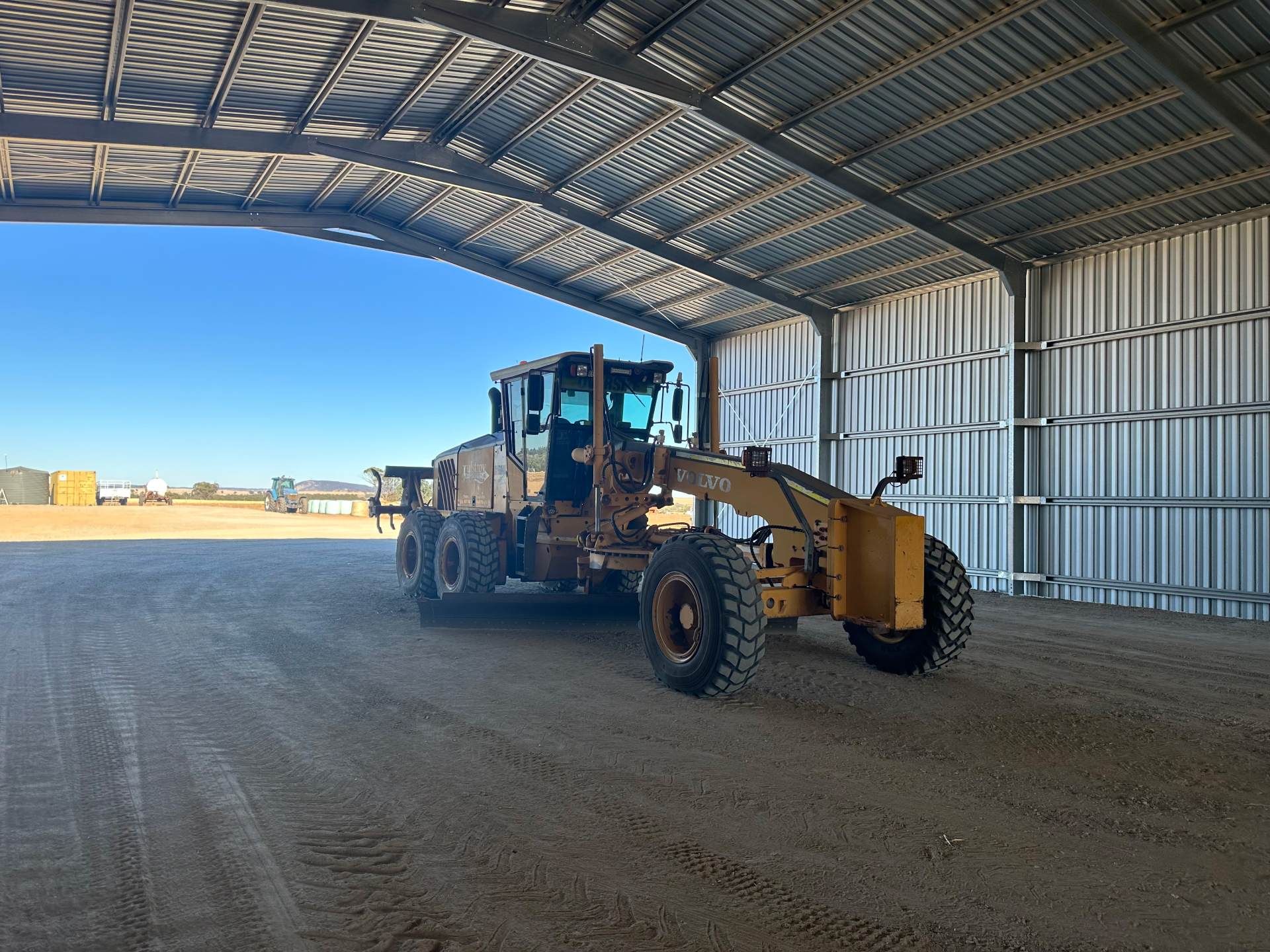 A large yellow tractor is parked inside of a metal building.