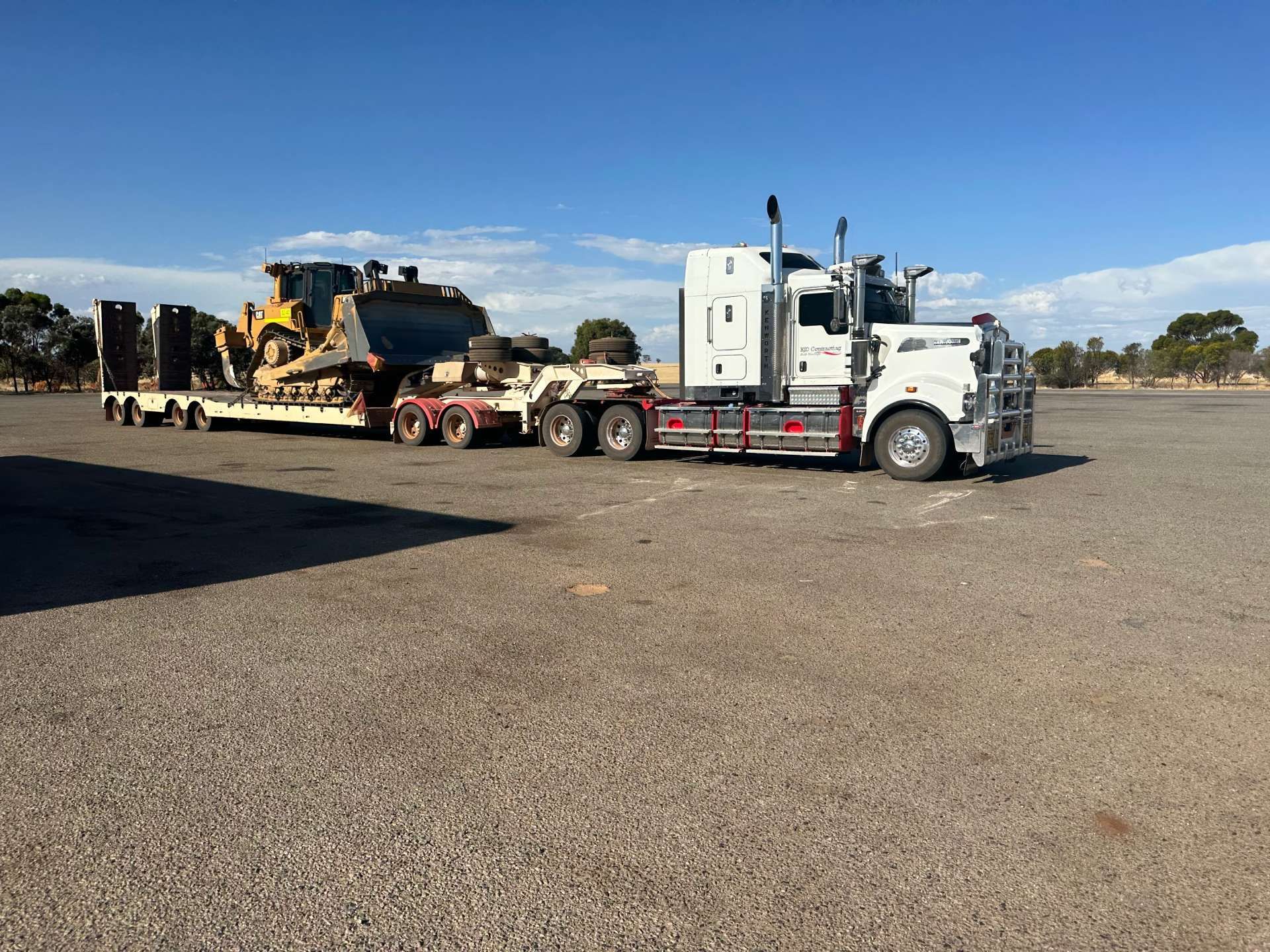 A white semi truck is carrying a bulldozer on a trailer.
