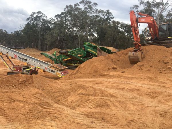 A large pile of dirt with a conveyor belt and an excavator in the background.
