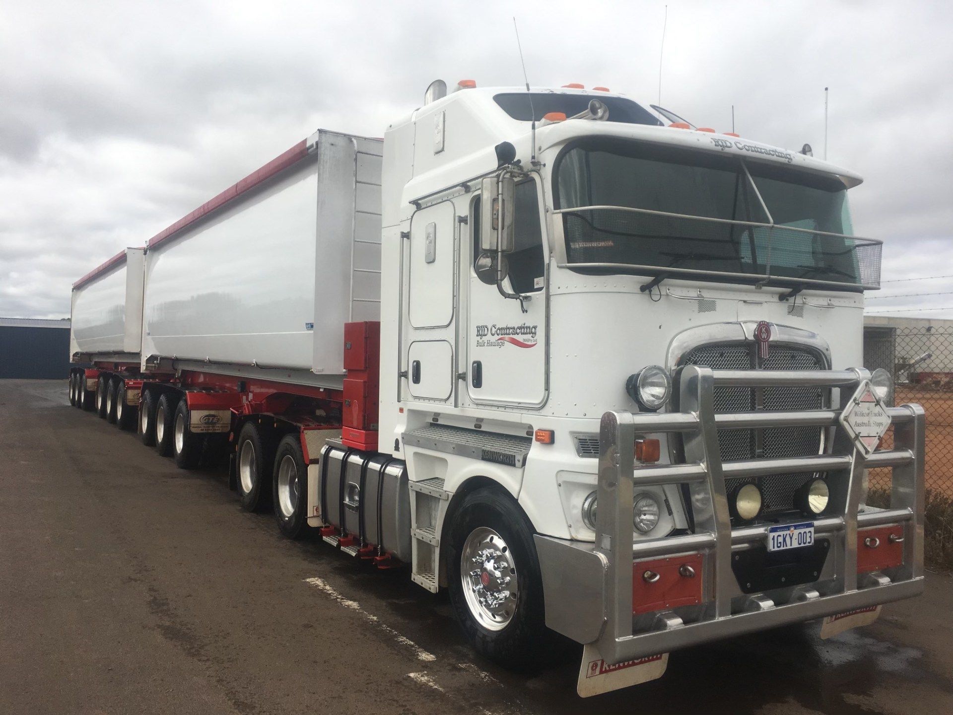 A white semi truck with a red trailer is parked in a parking lot.