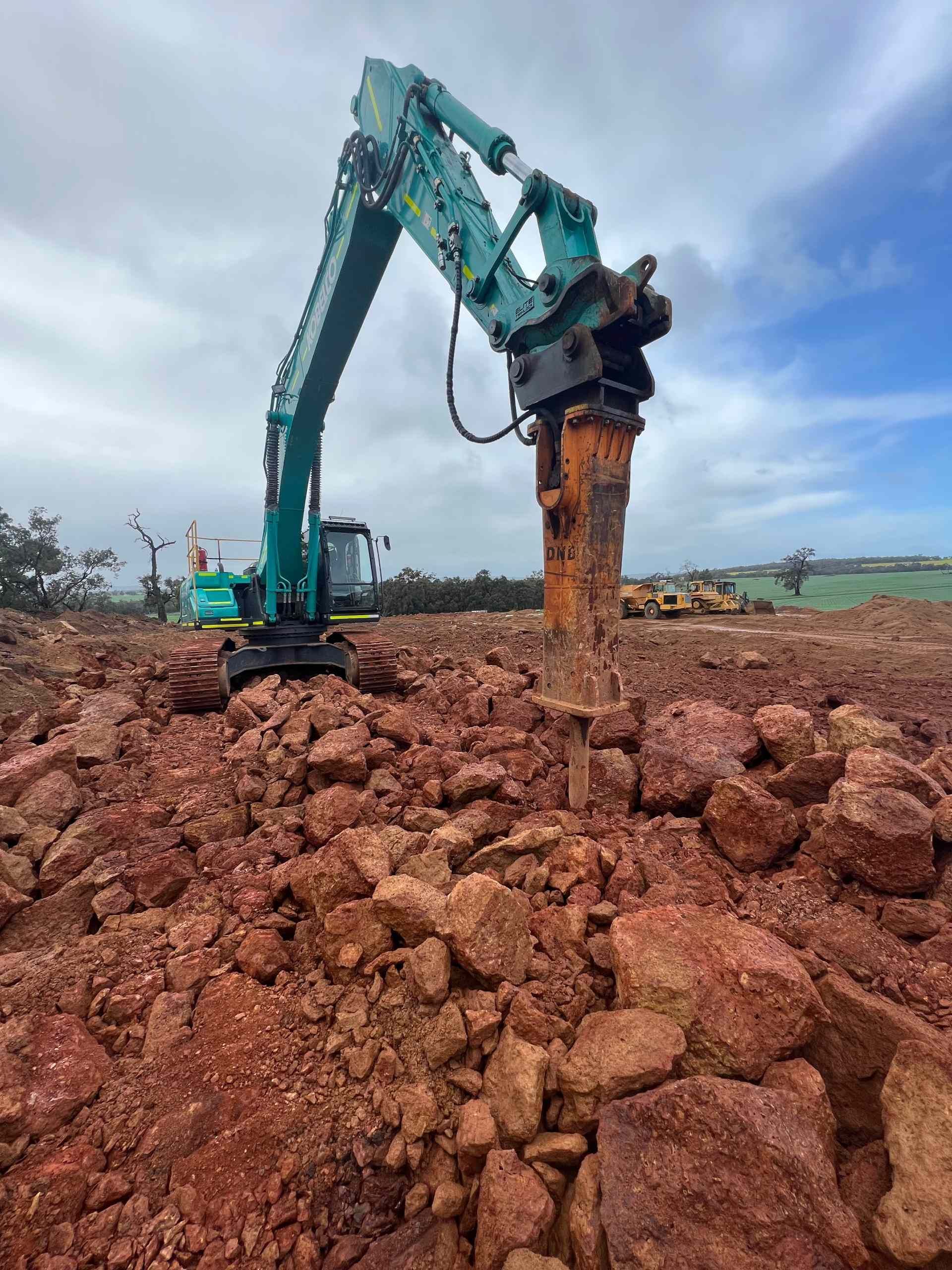 A large excavator is working on a pile of rocks in a field.