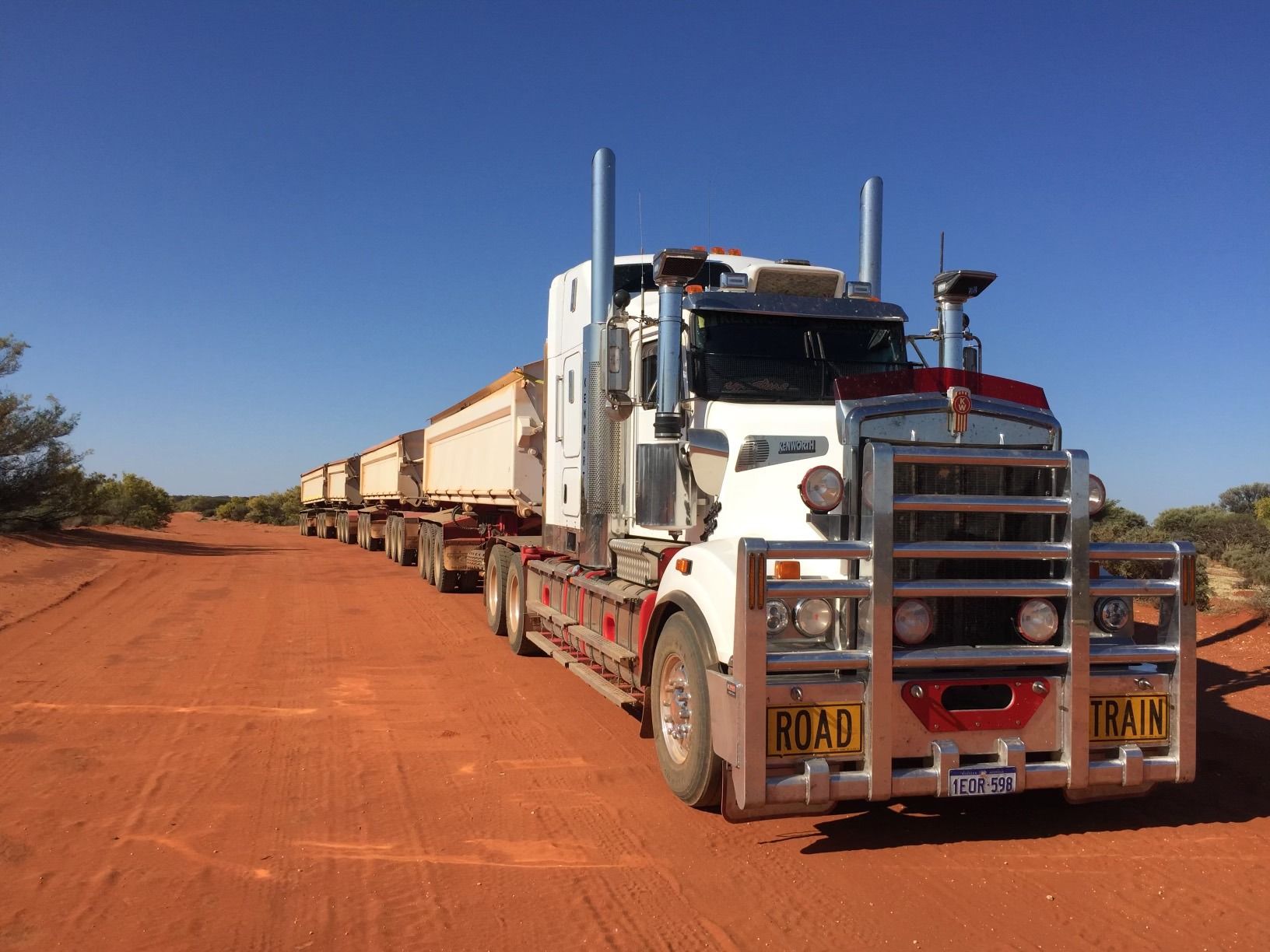 A white semi truck is parked on a dirt road.