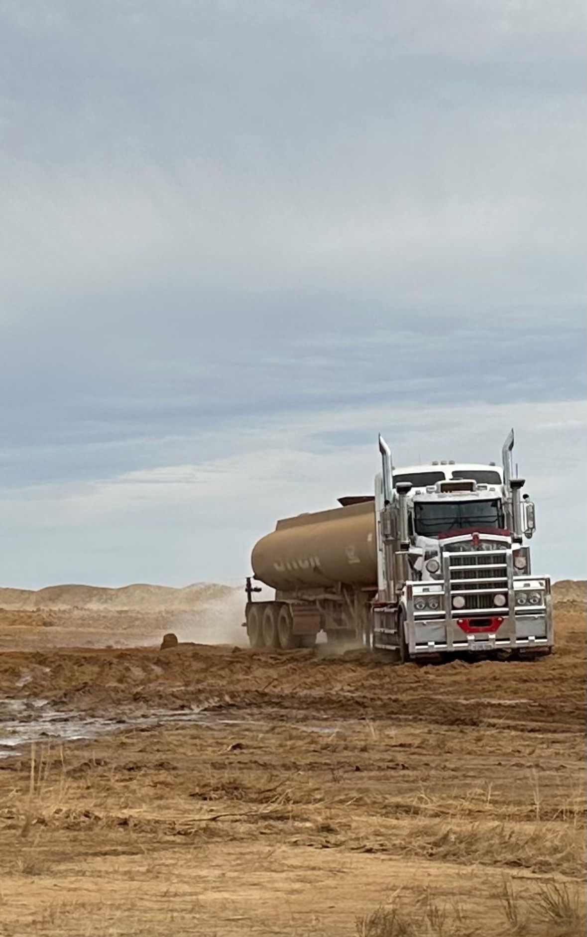 A semi truck is driving through a dirt field.