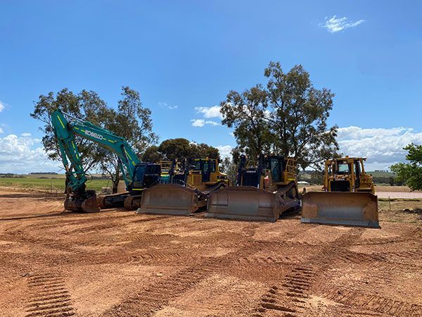 A group of construction vehicles are parked in a dirt field.