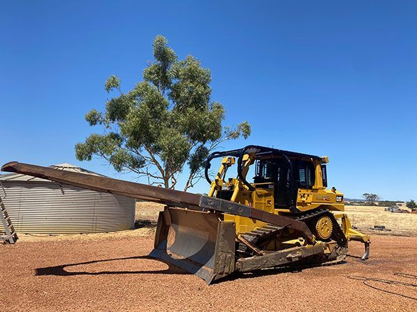 A bulldozer is parked in a dirt field with a tree in the background.