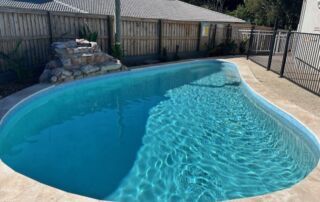 Backyard Swimming Pool with Clear Blue Water Beside a Fence and Stacked Rocks — Mad Pool Interiors and Renovations in Baringa, QLD